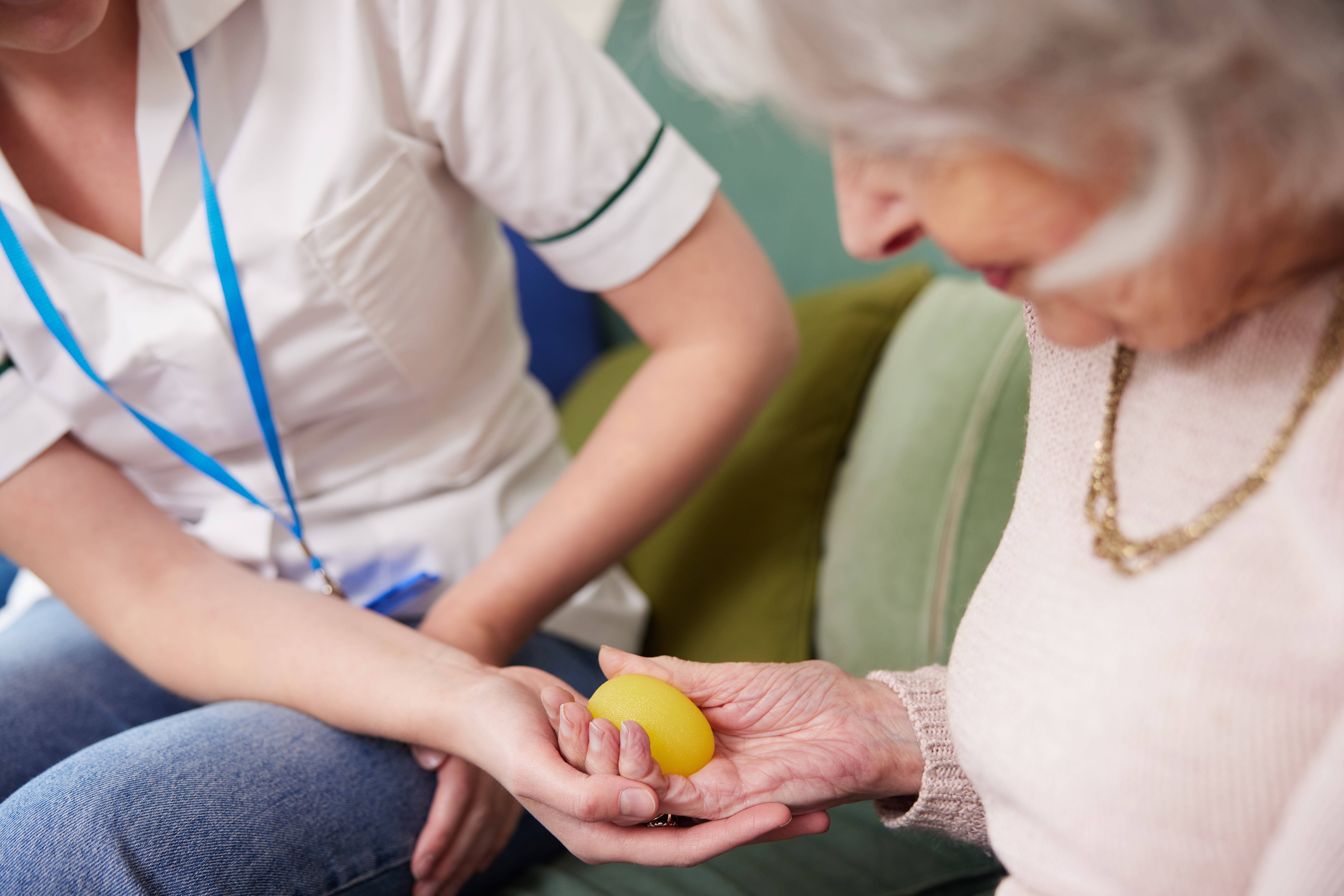 An occupational therapist helping an older woman squeeze a therapy ball in her hand.