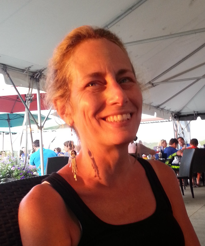 Headshot of Carol Hamer. Carol is smiling outside and is wearing a black tank top and long earrings.