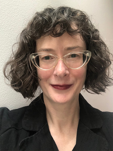 Headshot of Polly Abbott. Polly is wearing cat eye glasses and a black blazer.