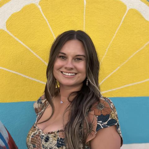 Headshot of Chandler McDaniel. She has brown hair and is smiling against a lemon backdrop.