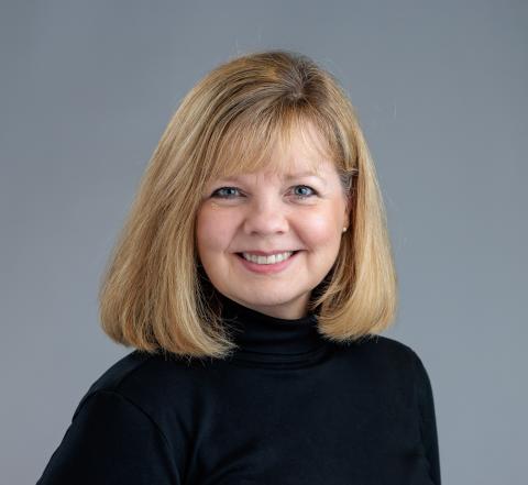Professional headshot of Alana Knudson. She is a middle-aged woman with short blond hair wearing a black turtleneck sweater.