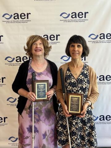 Jennifer and Kendra standing in front of an AER banner holding their awards and smiling.