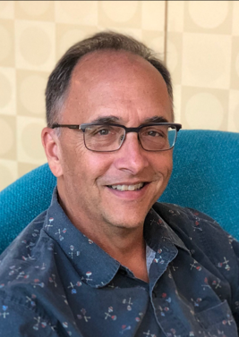 Headshot of Marty. Marty is a middle-aged man with glasses. He is smiling and wearing a navy blue collar shirt.