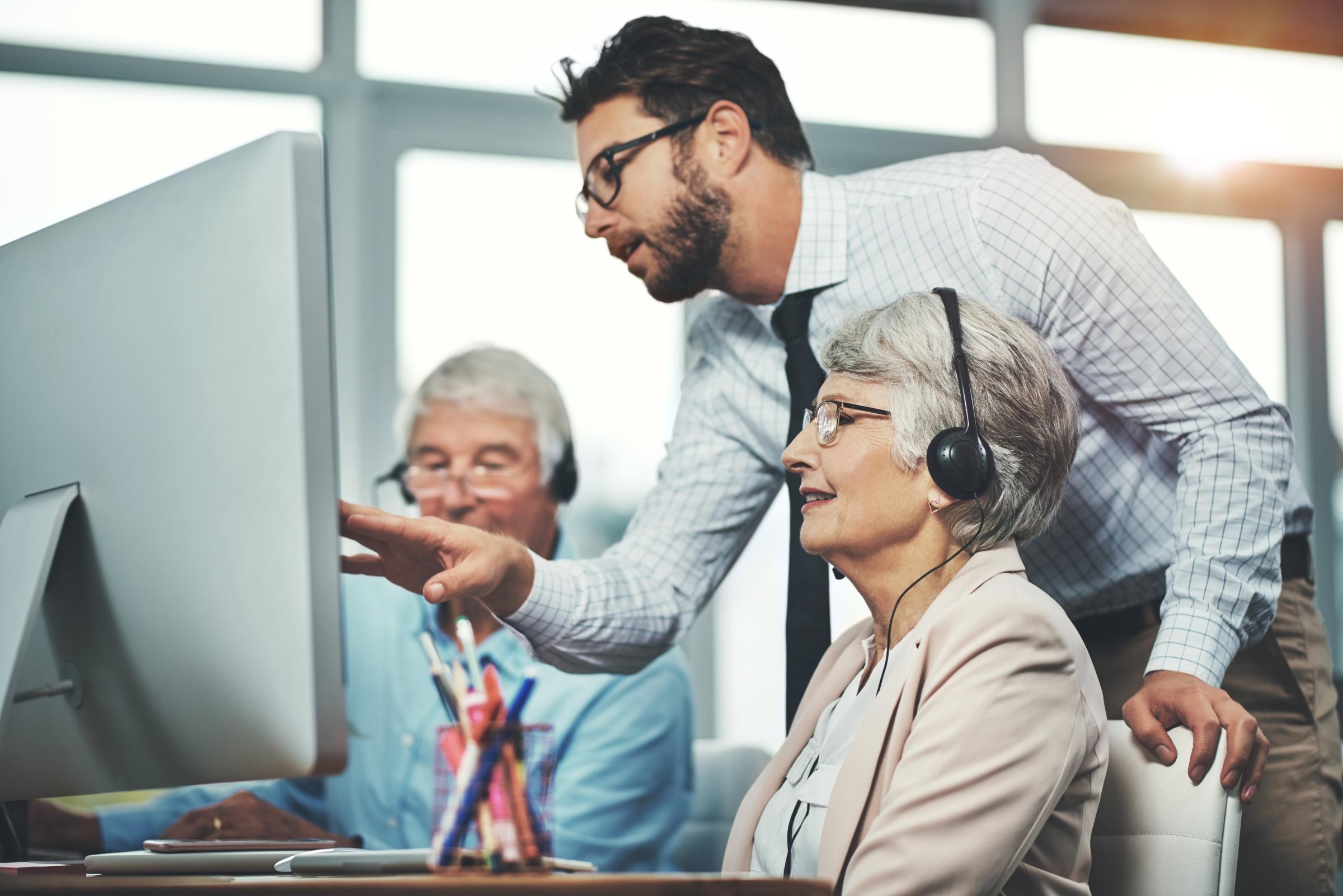 A helps an older woman with a task on her computer.