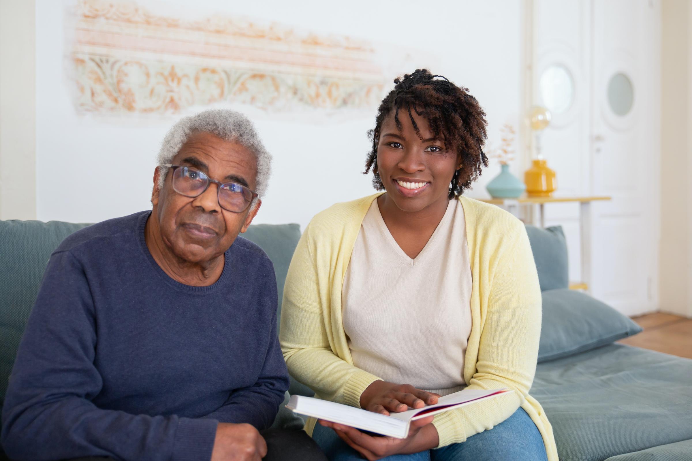 An older black man sits next to a black woman on a blue leather couch.