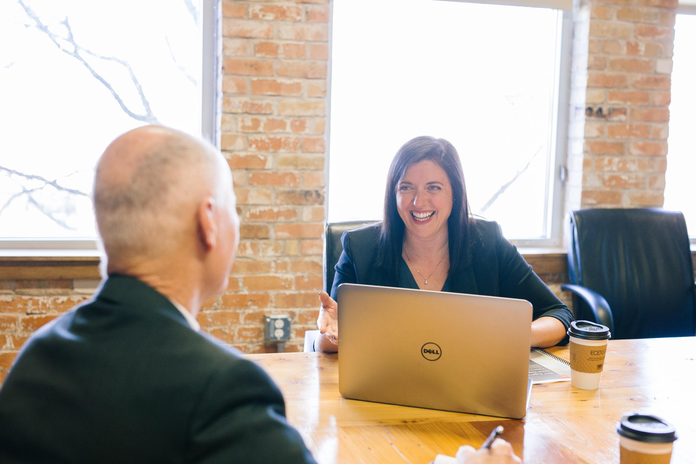 A woman helps an older man with a task on her computer.