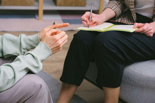 A close-up of a counselor writing down notes in a green notebook with her patient sitting in front of her.