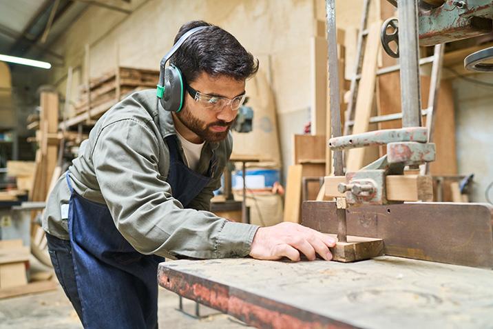 Man wearing earmuffs cutting wood using a saw.