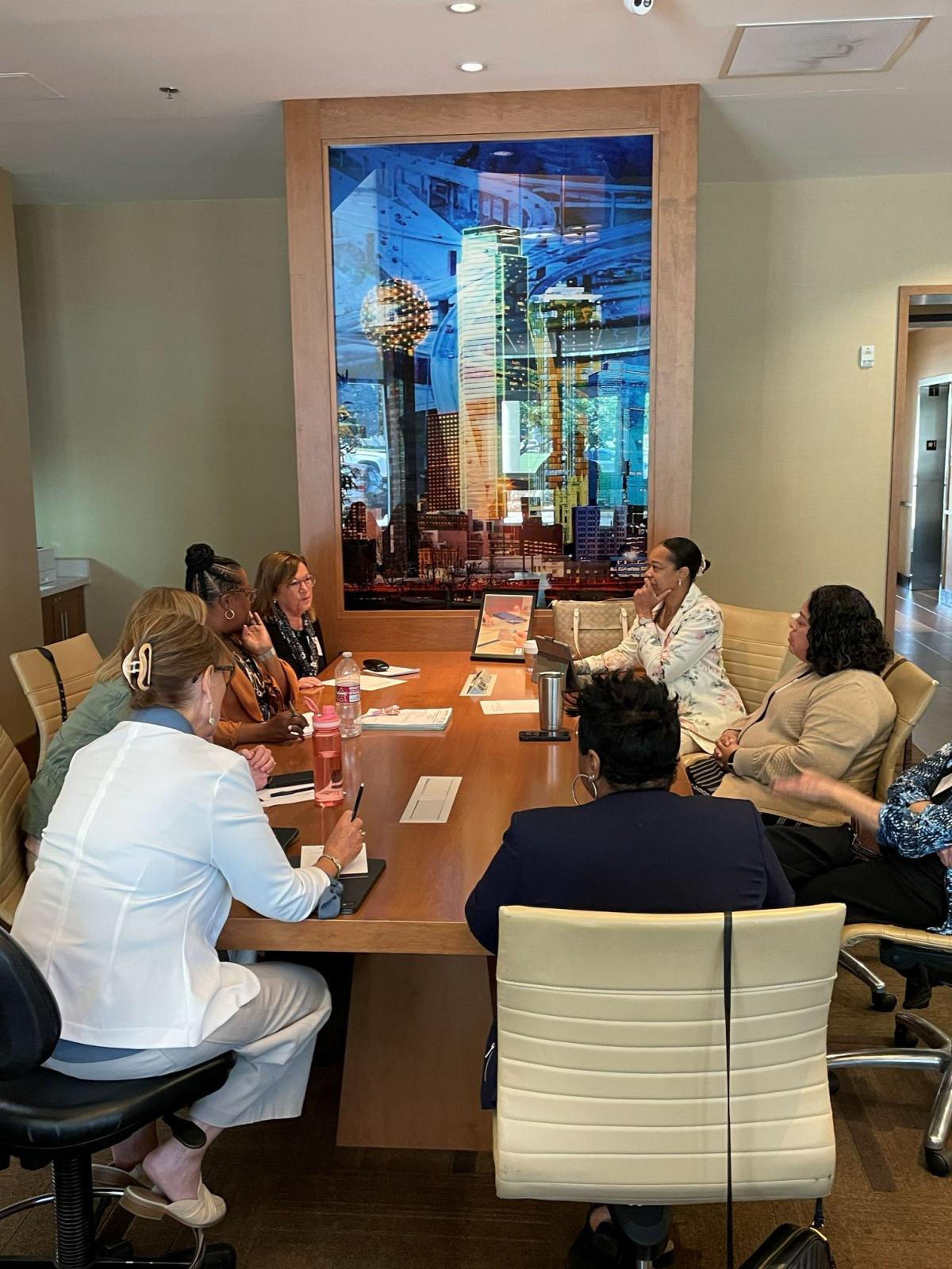 Attendees speaking to each other at the conference at a table. A pictures of the Reunion Tower is on the wall facing the conference table.
