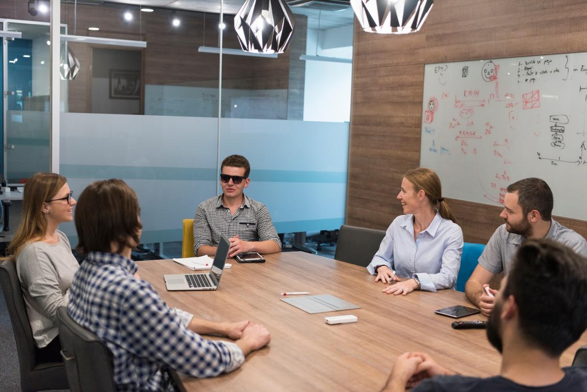 Business team meeting. A man wearing sunglasses sits at the front of the table