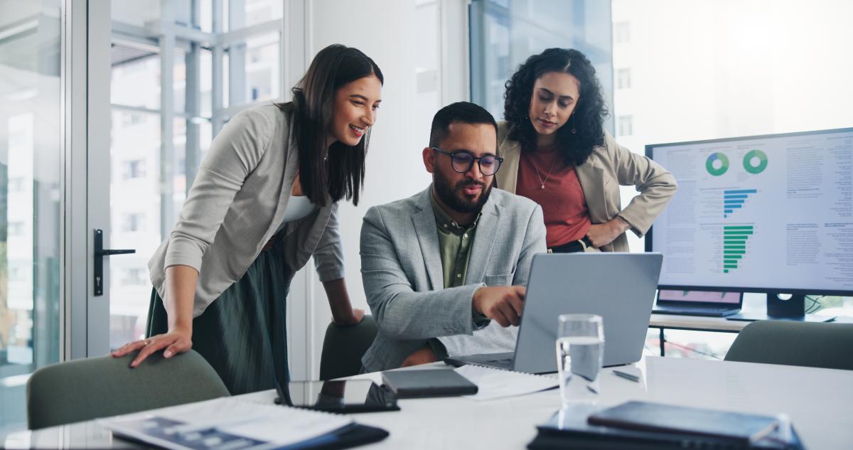 Three employees together looking at a coworker's laptop and discussing ideas in an office.