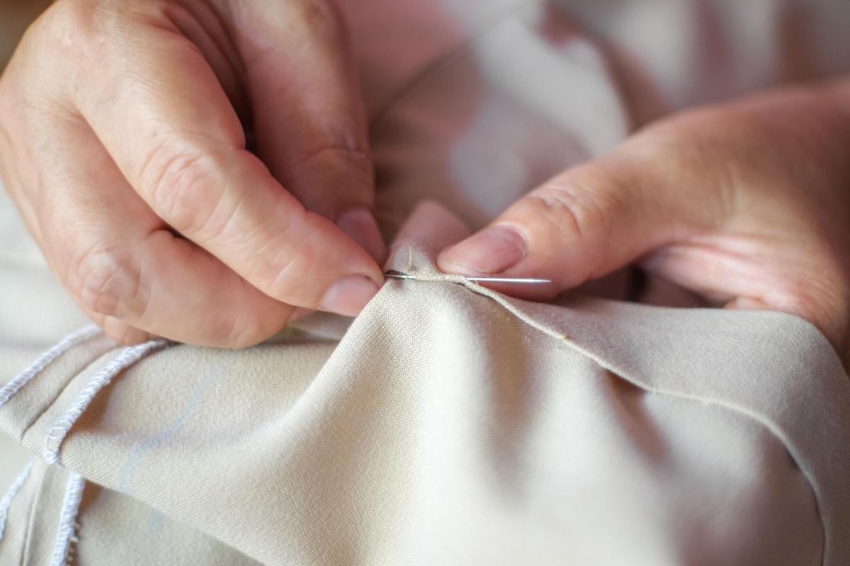 Person sewing beige slacks using a needle.