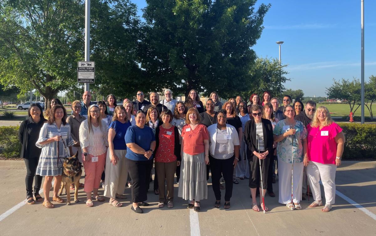 Group photo of OIB-TAC conference attendees smiling outside in a hotel parking lot.